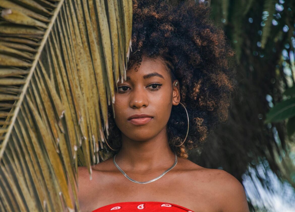 woman wearing silver colored hoop earrings and necklace behind green palm tree leaf